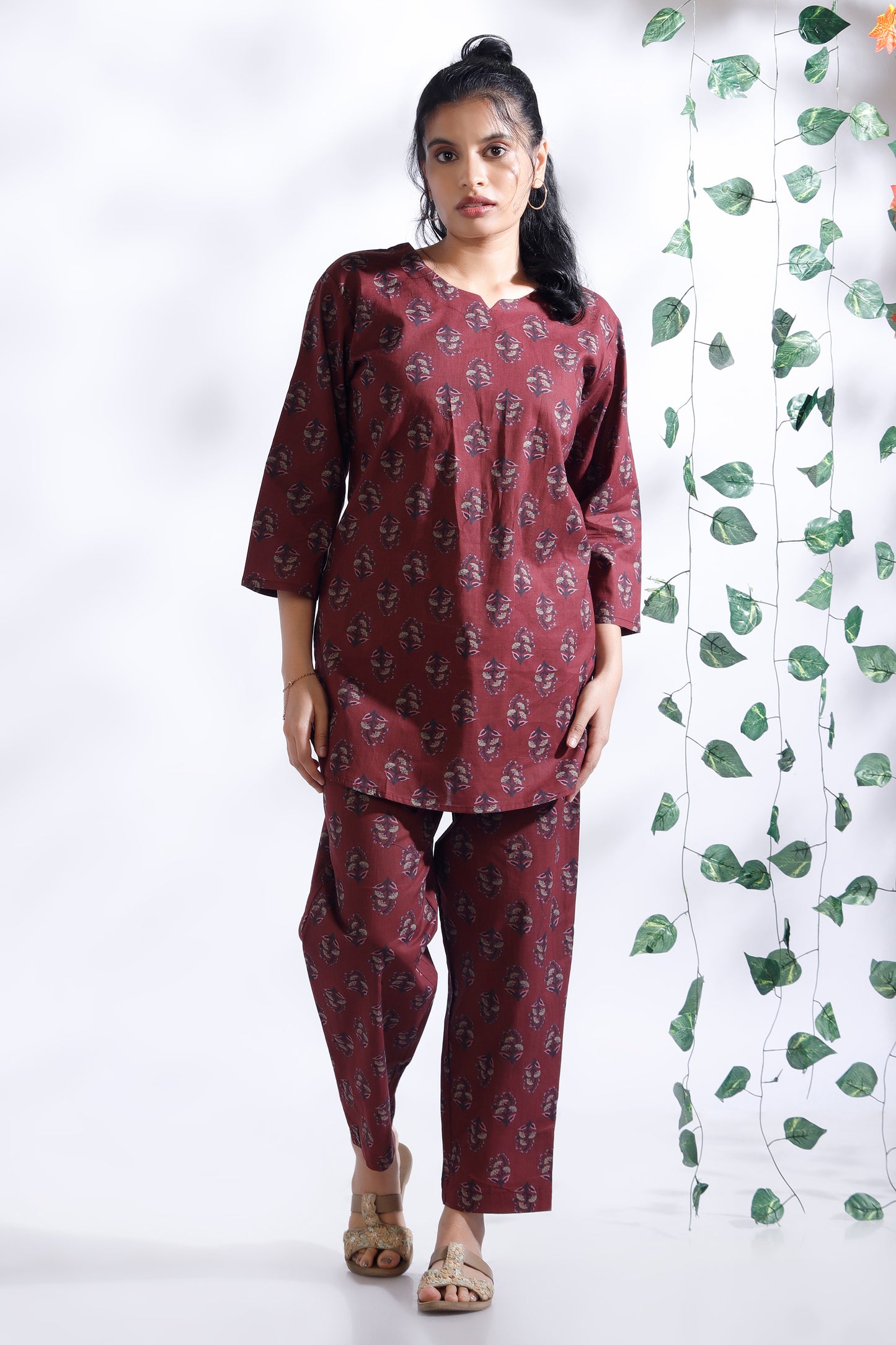 Woman wearing a maroon printed outfit with a white background and green leafy decoration.