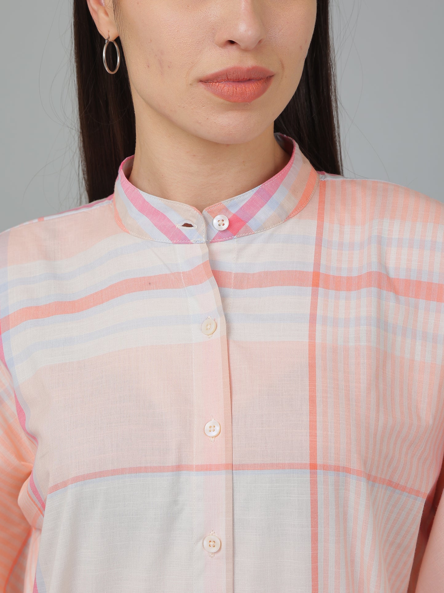 Person wearing a light pink and white checkered shirt with a neutral background
