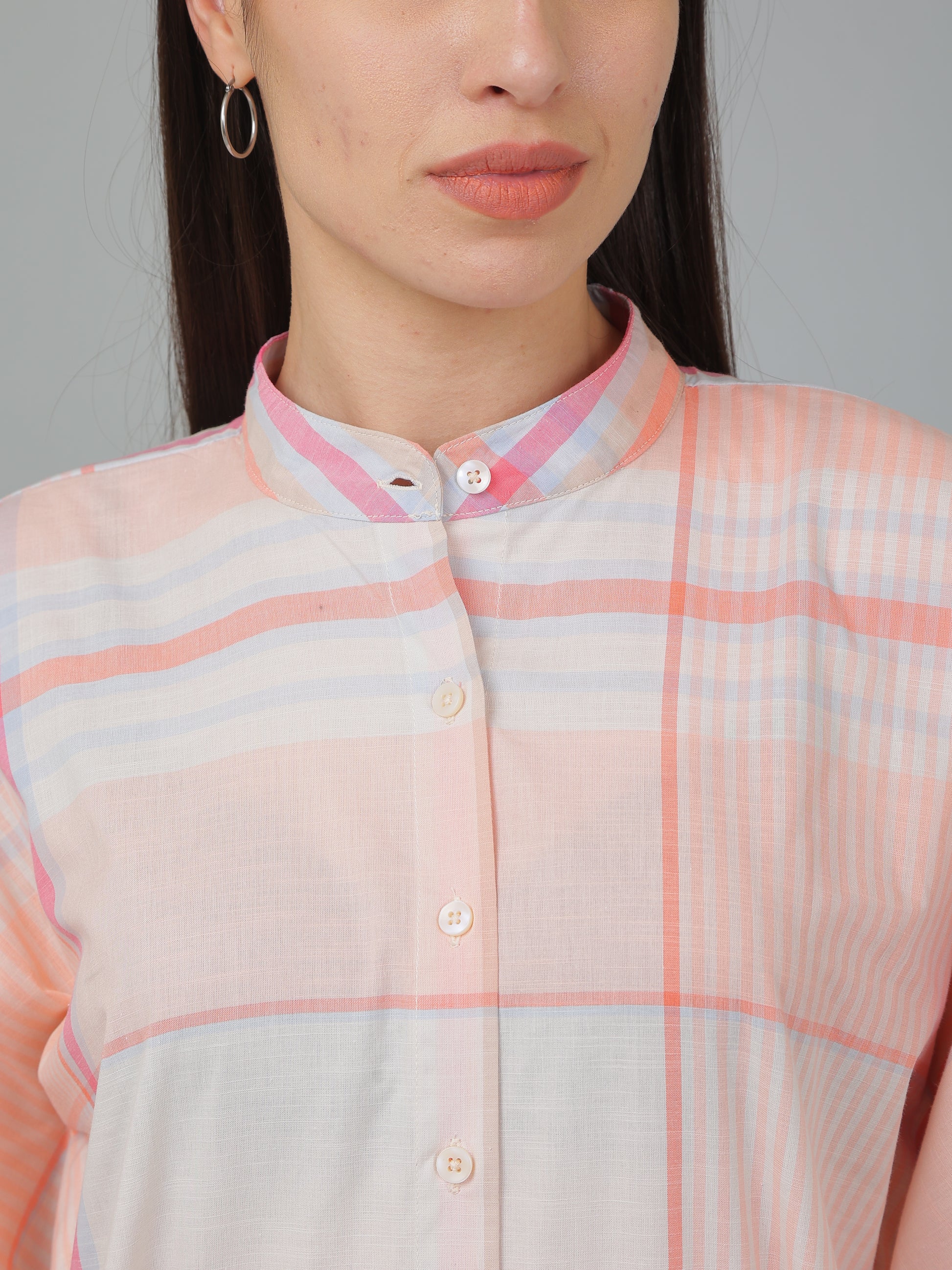 Person wearing a light pink and white checkered shirt with a neutral background