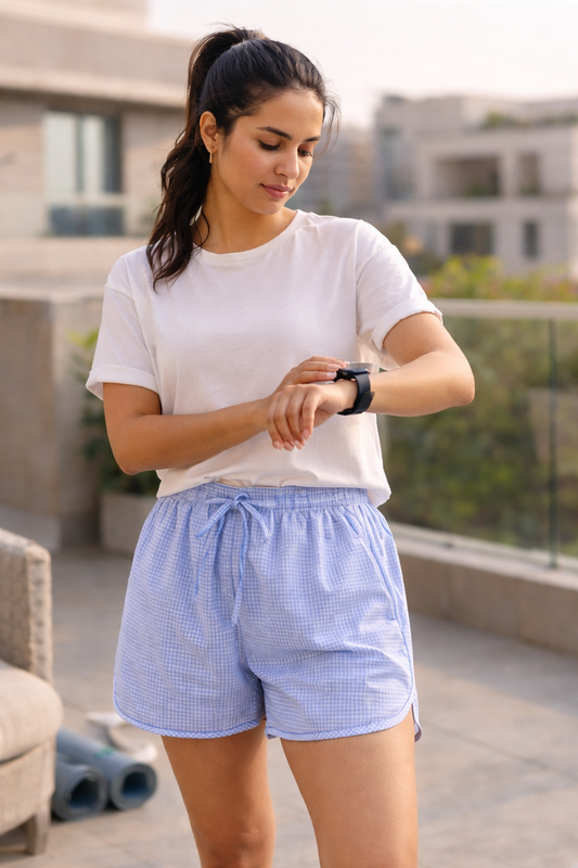 Woman wearing a white t-shirt and blue checkered shorts, checking her watch on a rooftop.