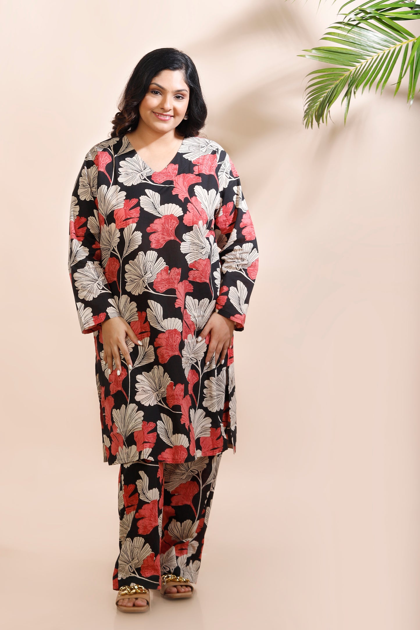 Woman wearing a floral dress against a beige wall with a plant.