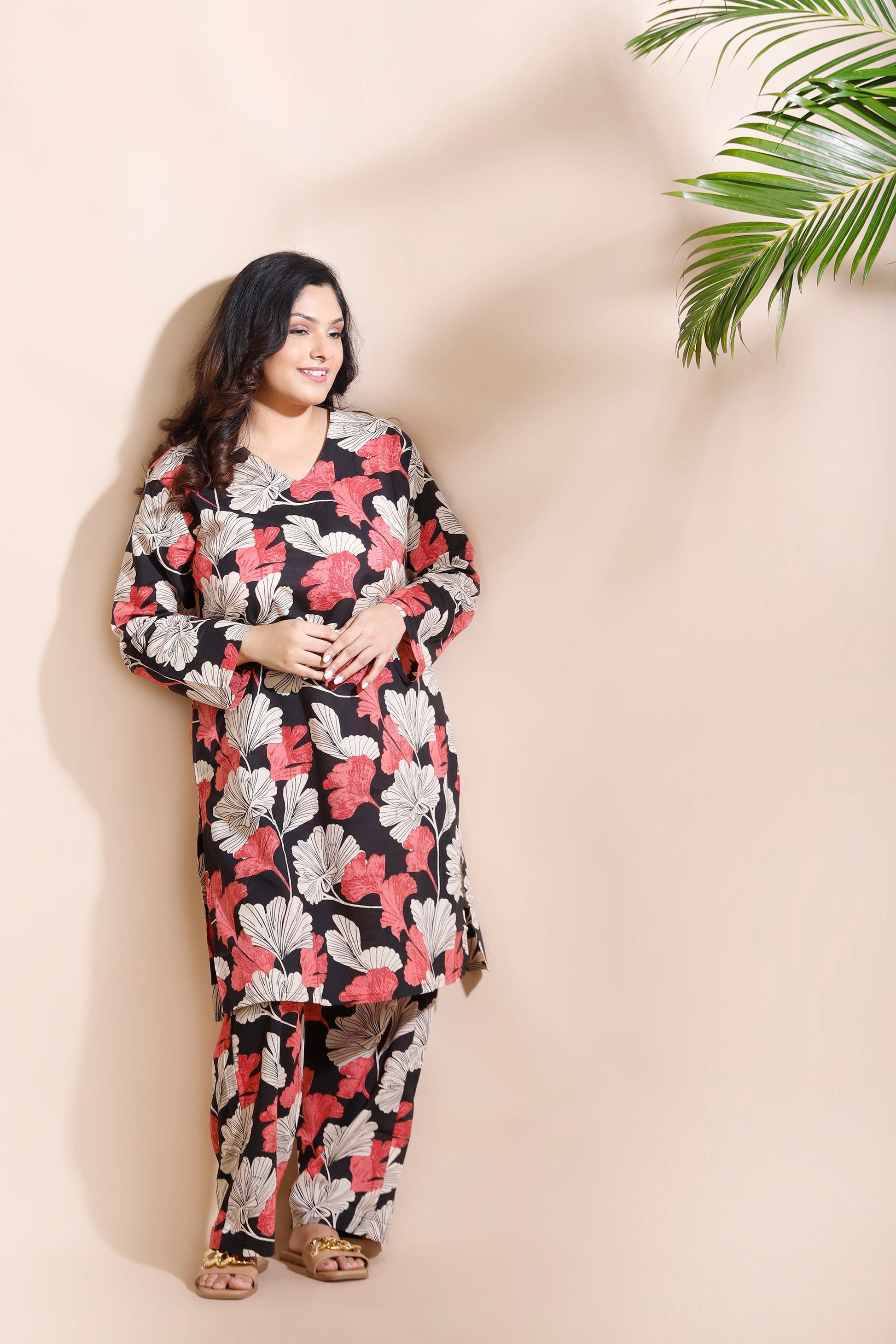 Woman wearing a floral dress against a beige wall with a plant.