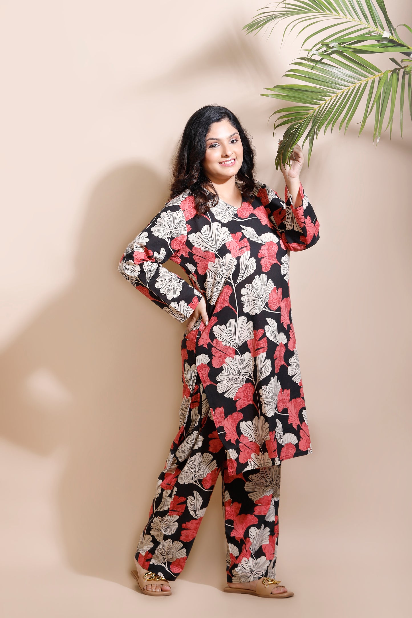 Woman wearing a floral dress against a beige wall with a plant.