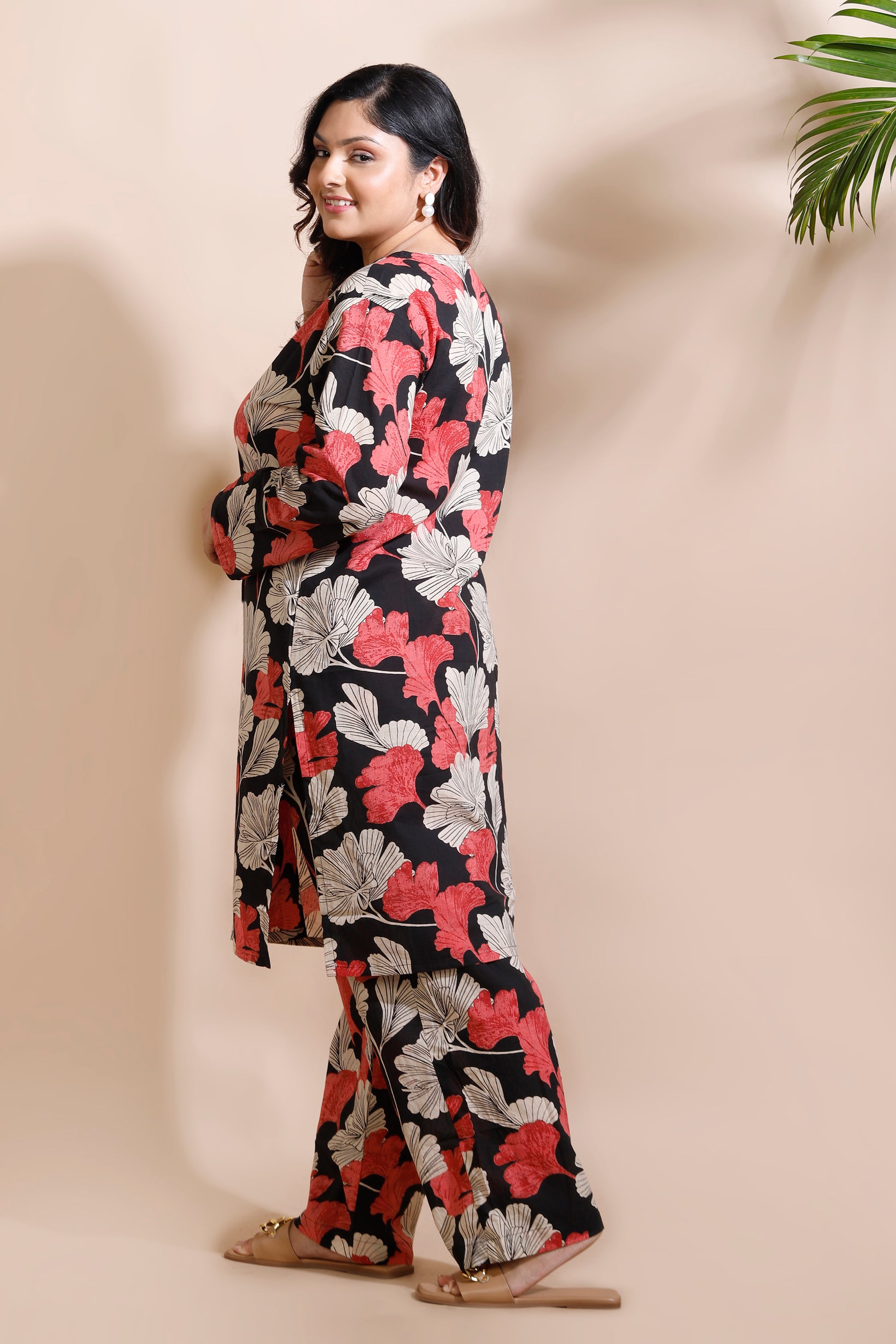 Woman wearing a floral dress against a beige wall with a plant.