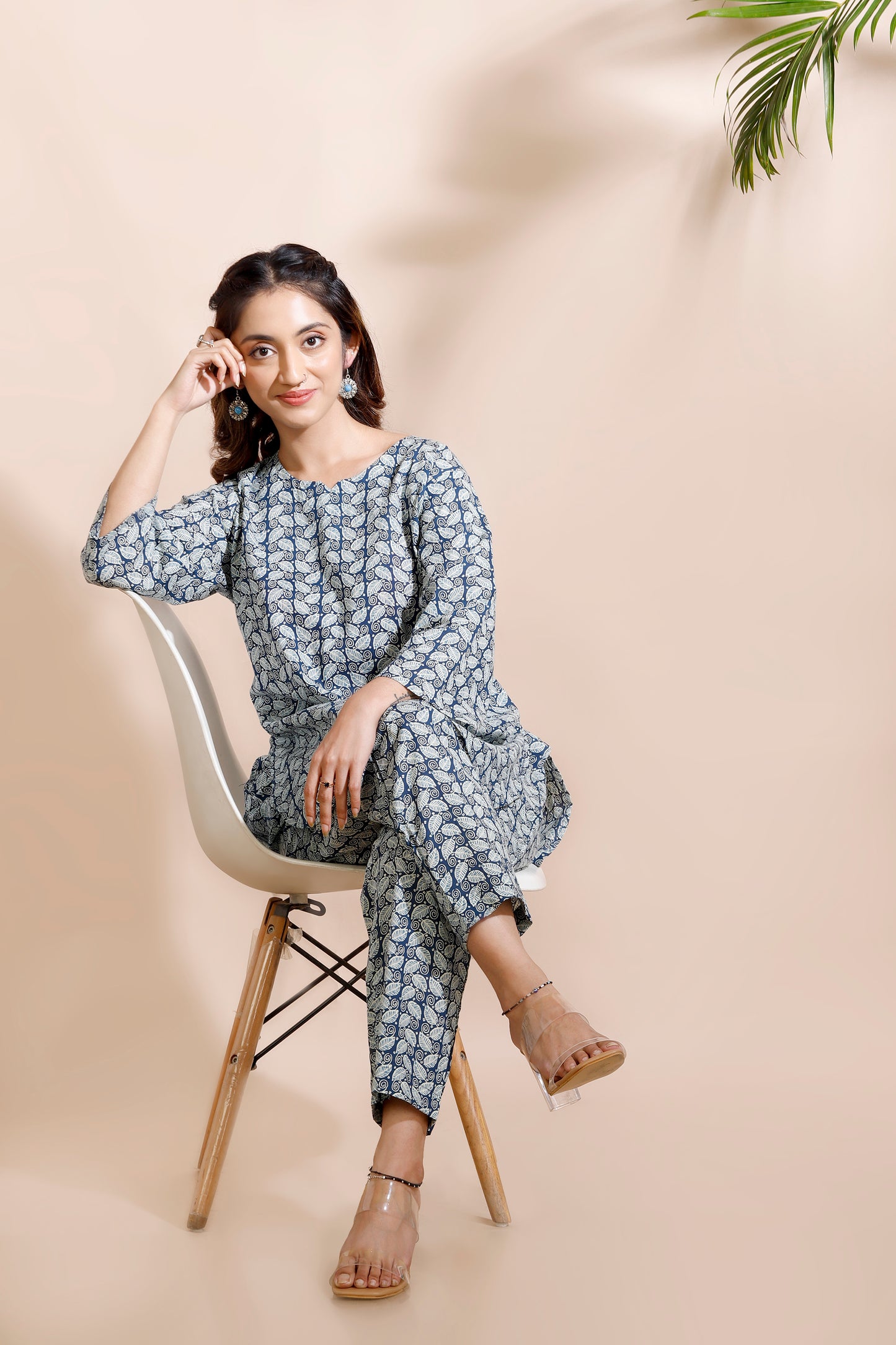 Woman sitting on a chair wearing a blue floral outfit against a beige background