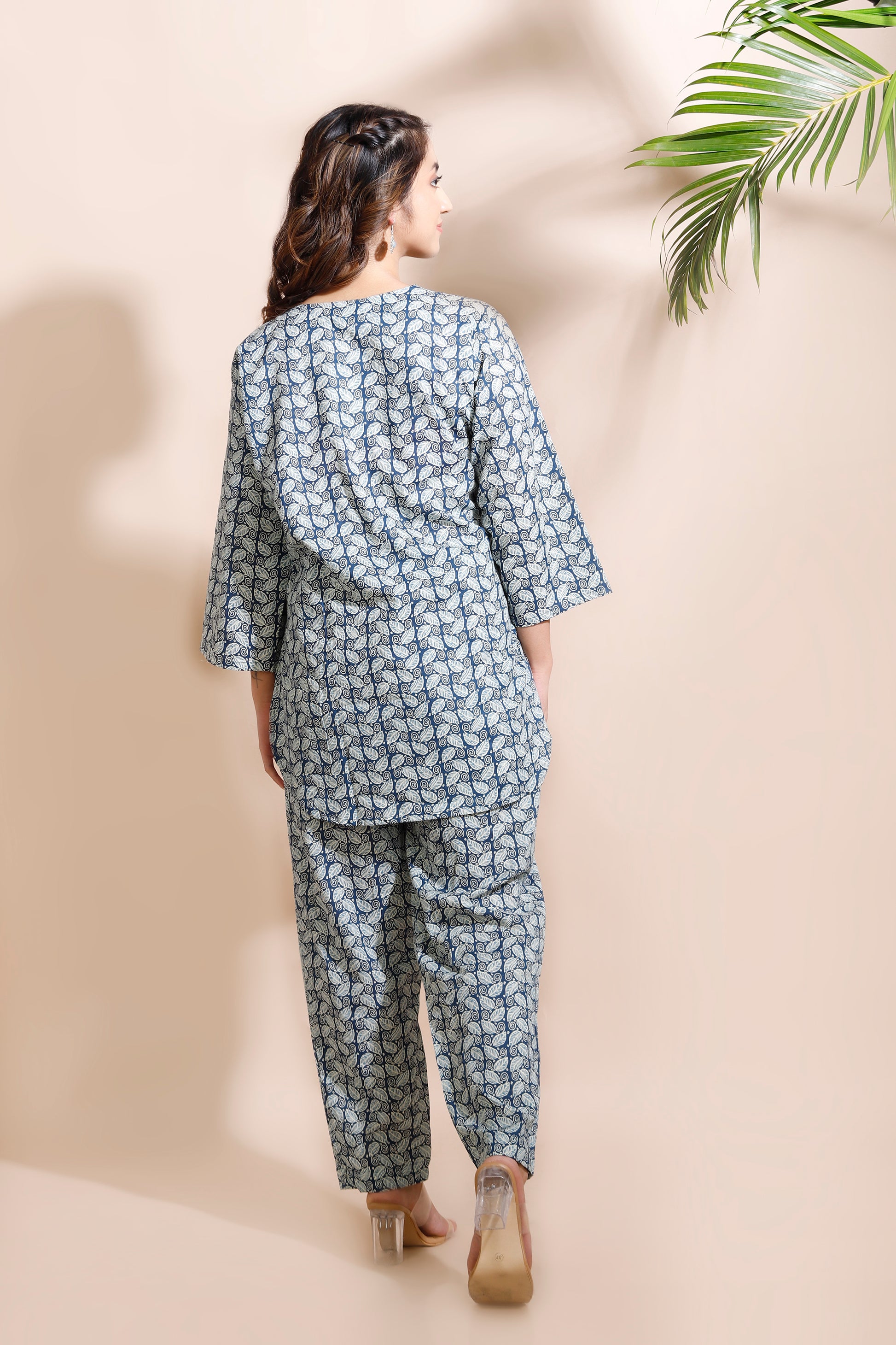 Woman wearing a matching top and pants set with a leaf pattern against a beige background