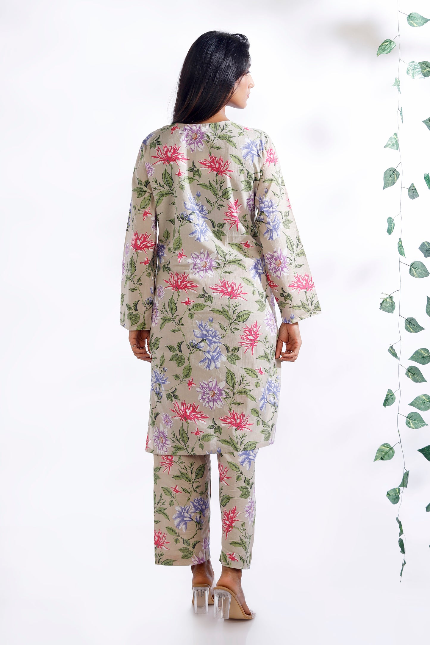Woman wearing a floral outfit standing next to a plant on a white background