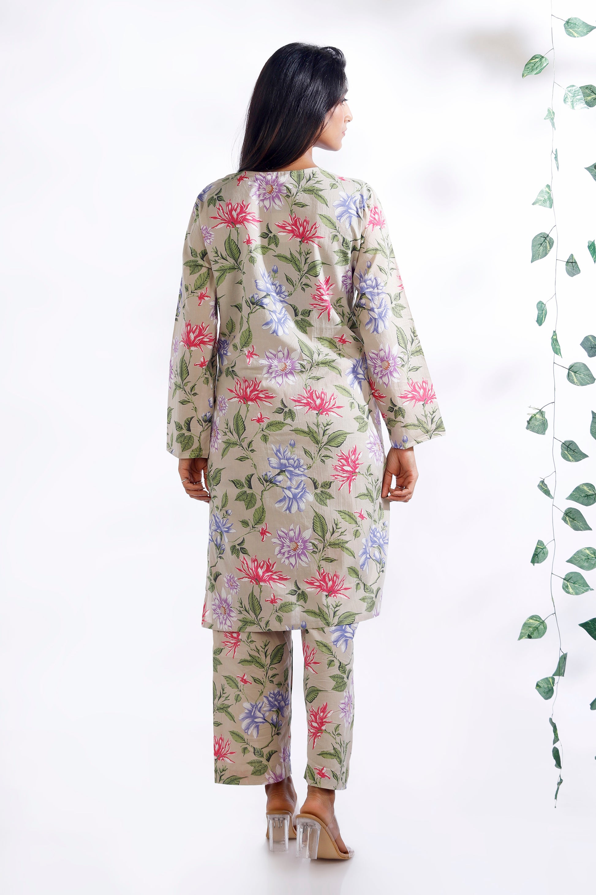 Woman wearing a floral outfit standing next to a plant on a white background
