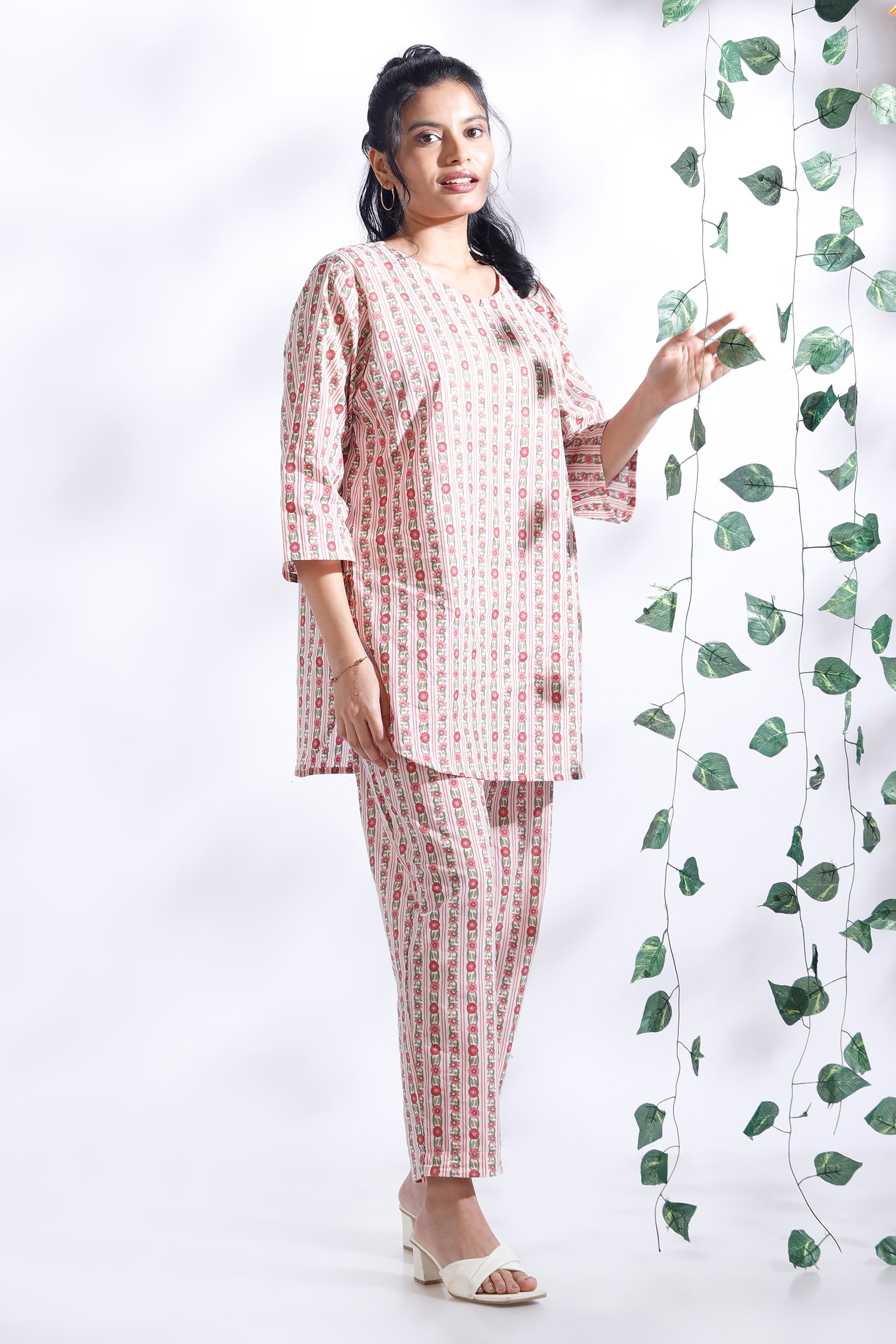 Woman in a pink and white checkered outfit standing next to a decorative plant on a white background
