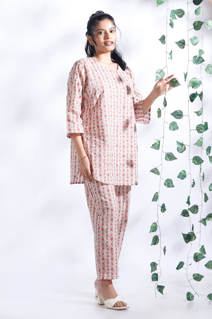 Woman in a pink and white checkered outfit standing next to a decorative plant on a white background