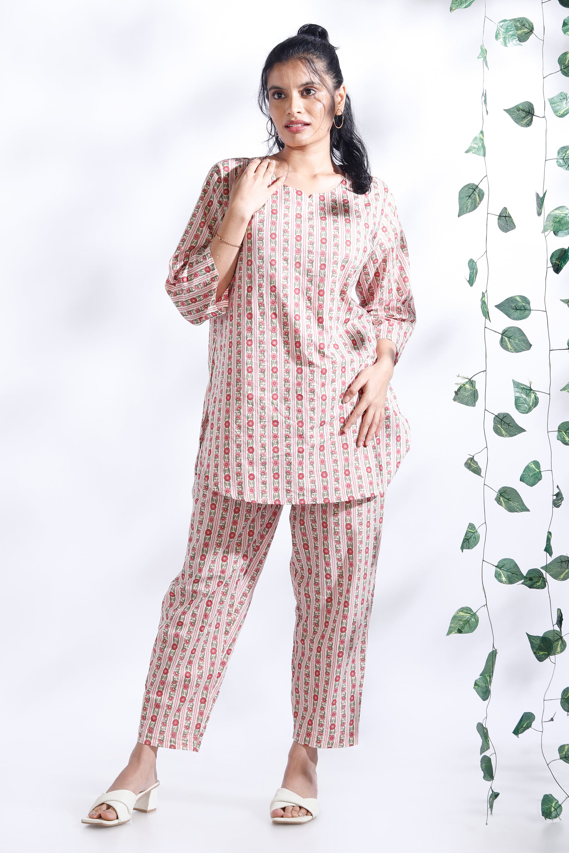 Woman wearing a matching set of kurta and pants with a white background and green leaves.