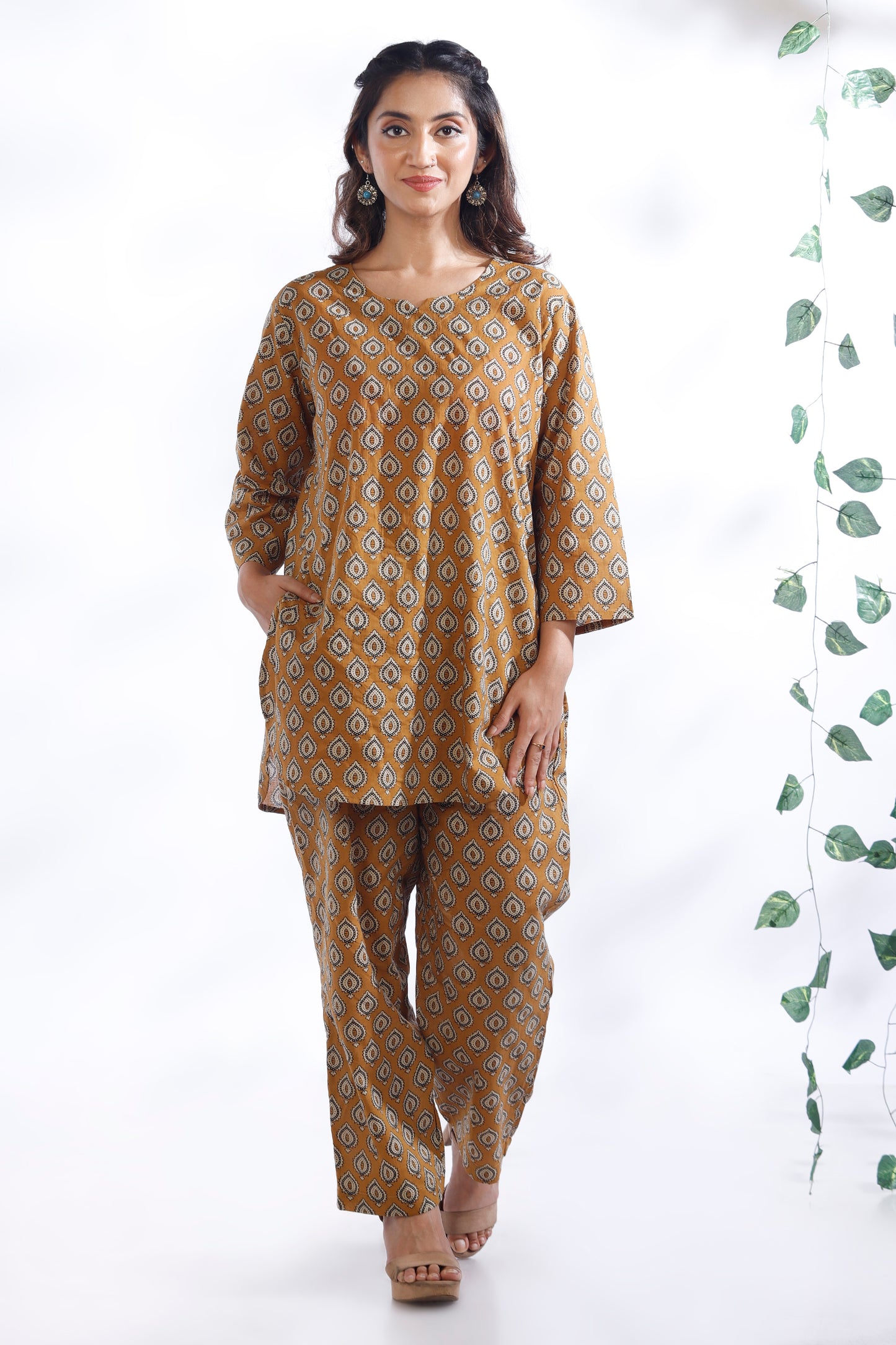 Woman wearing a mustard yellow patterned kurta with palazzo pants on a white background