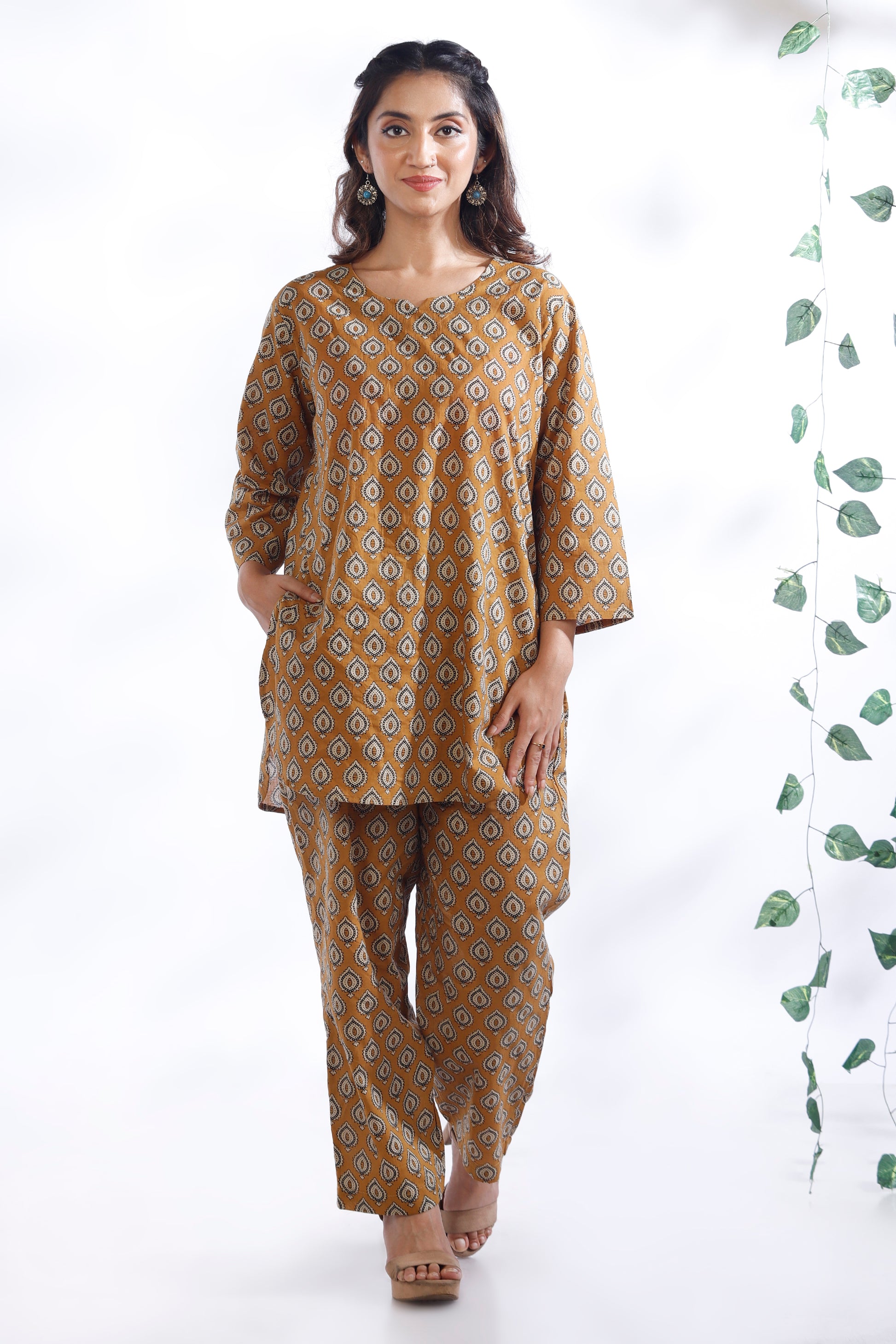 Woman wearing a mustard yellow patterned kurta with palazzo pants on a white background