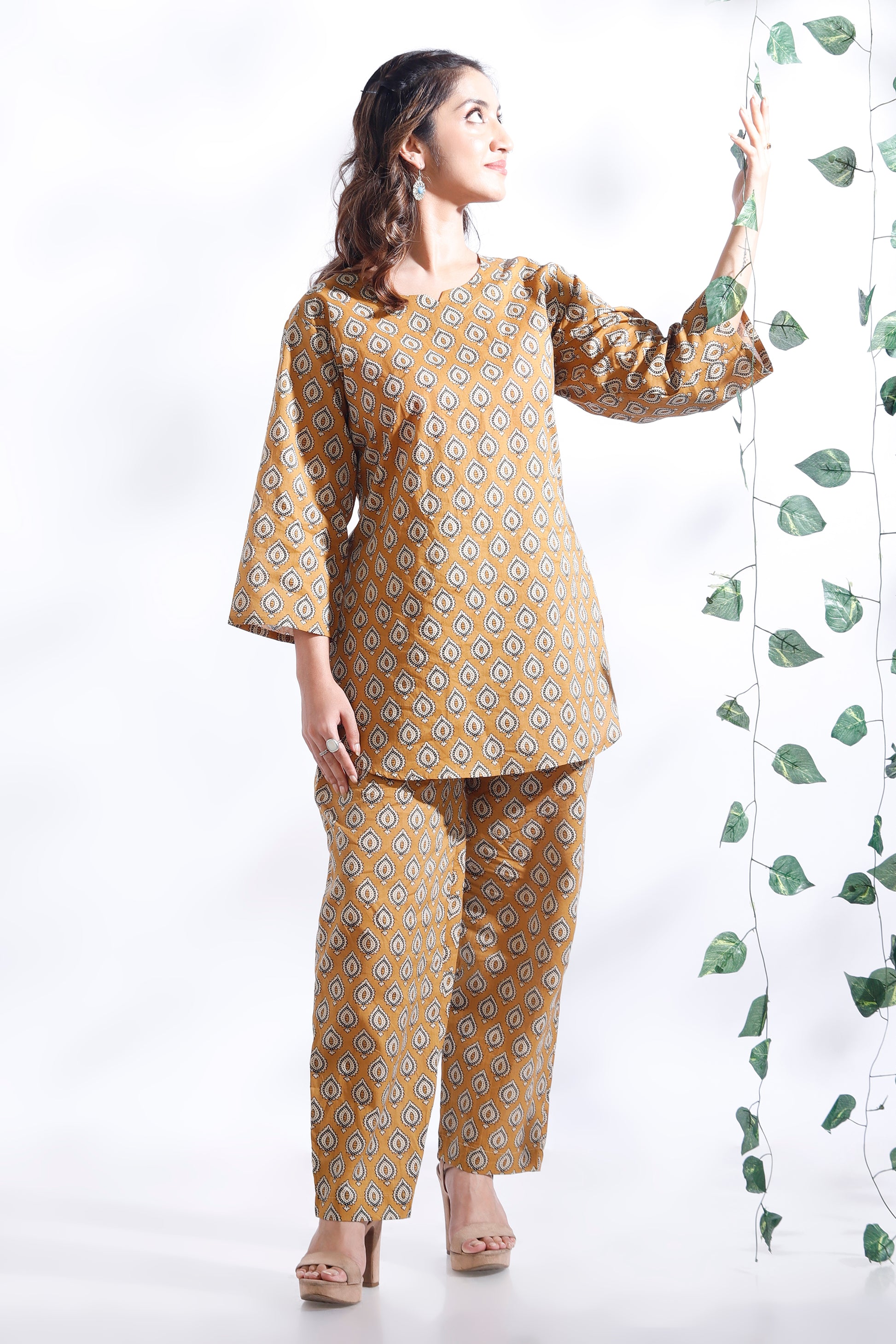Woman wearing a mustard yellow floral outfit against a white background with green leaves.