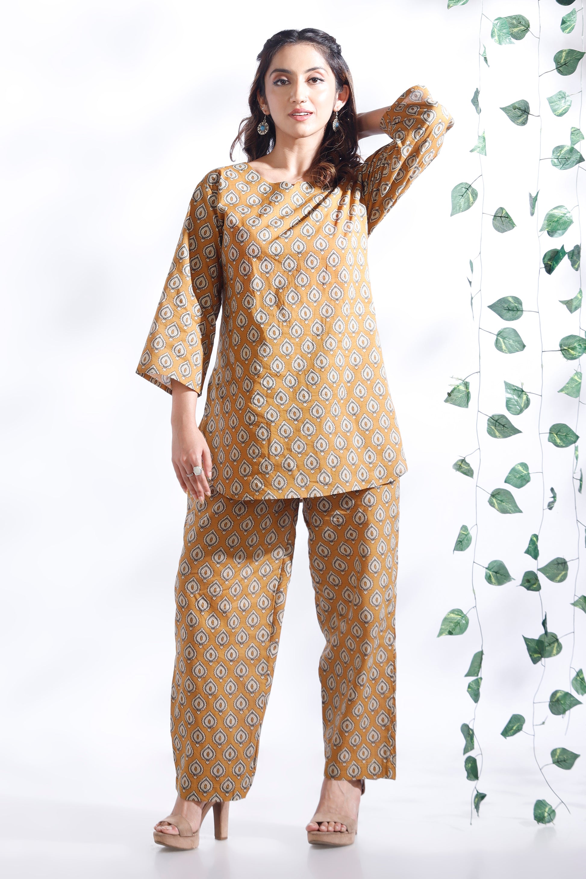 Woman wearing a mustard yellow patterned outfit with a white background