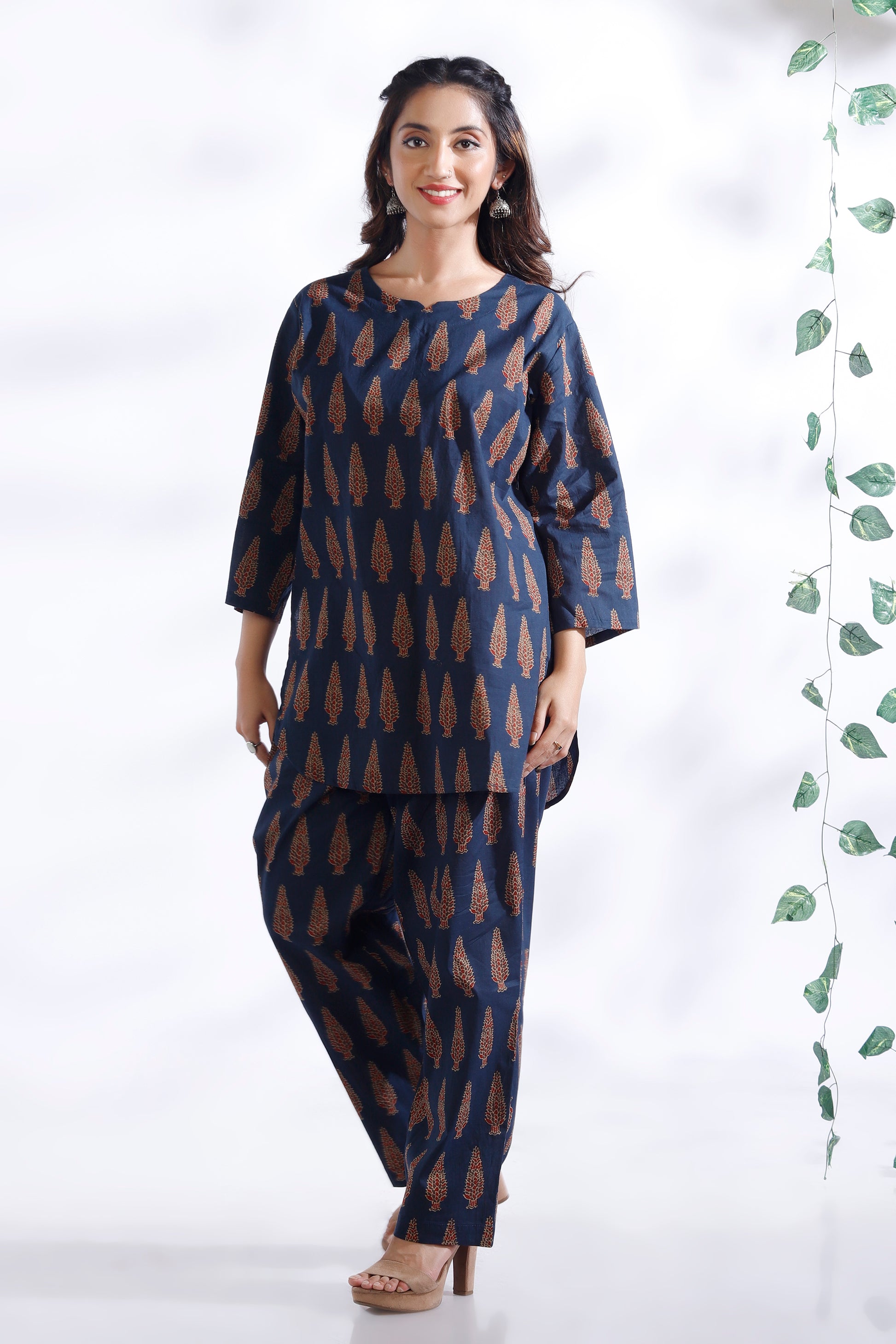 Woman wearing a navy blue patterned outfit with a white background and green leaves.