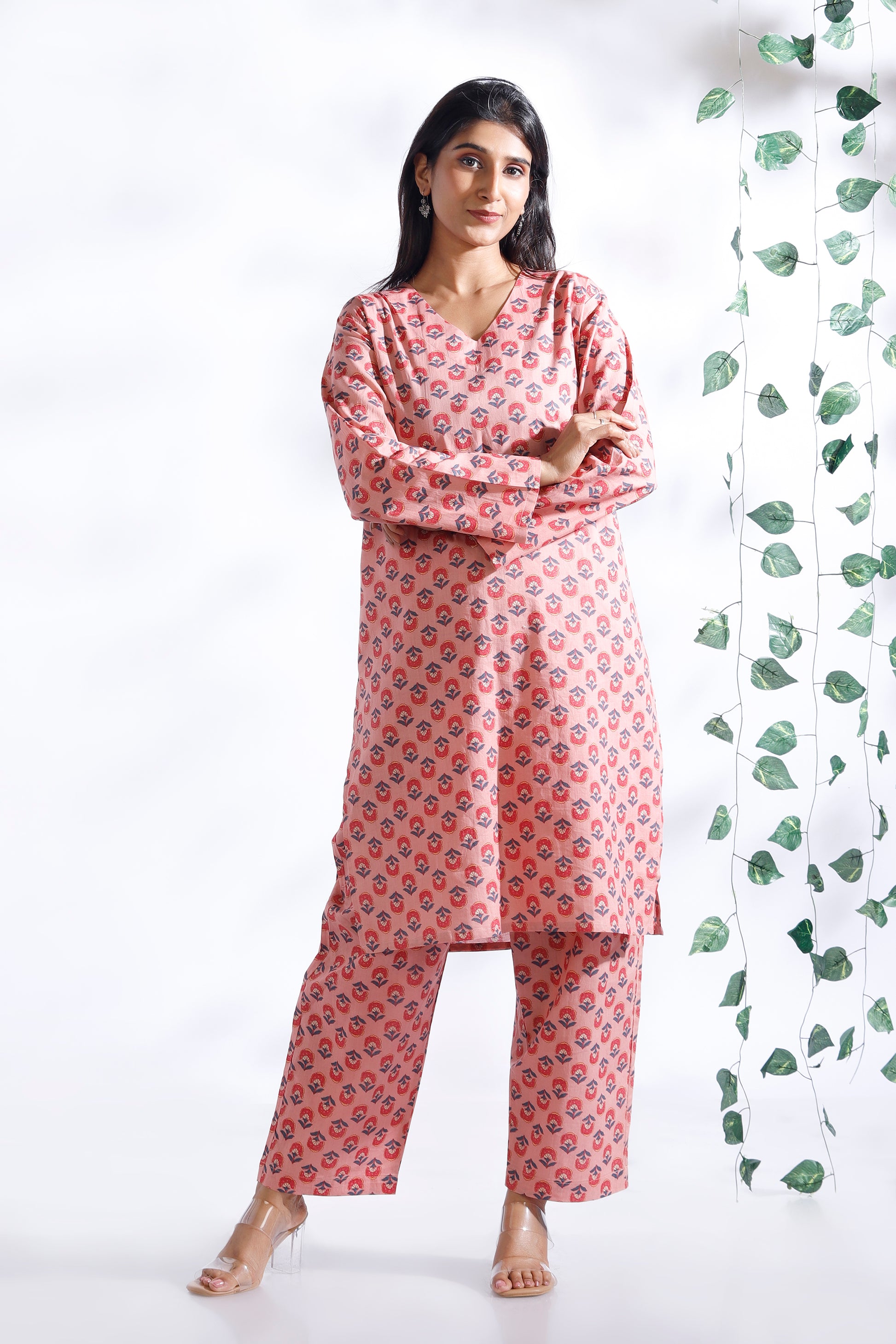 Woman wearing a pink floral outfit standing against a white background with green leaves.
