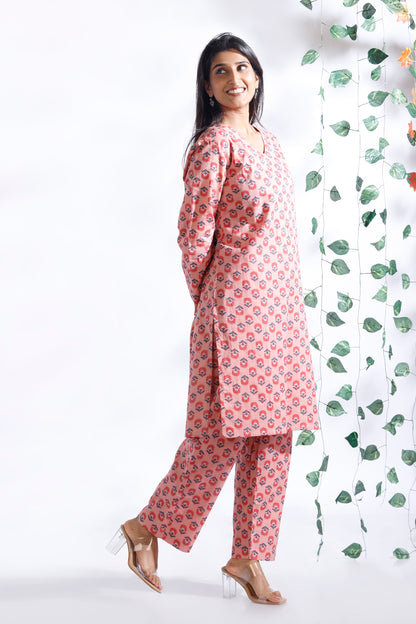 Woman wearing a pink floral outfit standing next to a decorative plant against a white background
