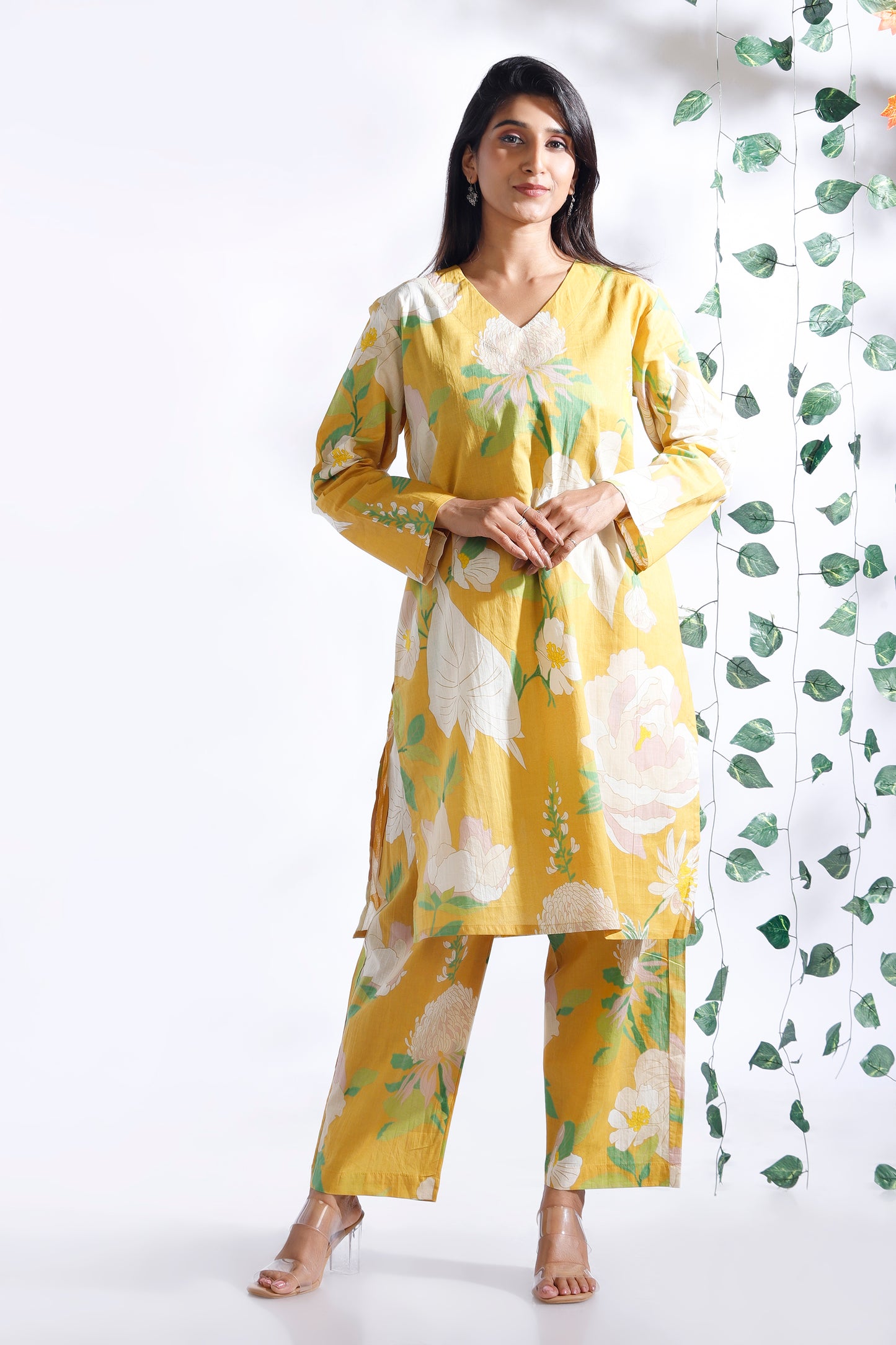 Woman wearing a yellow floral outfit against a white background with green leaf patterns.