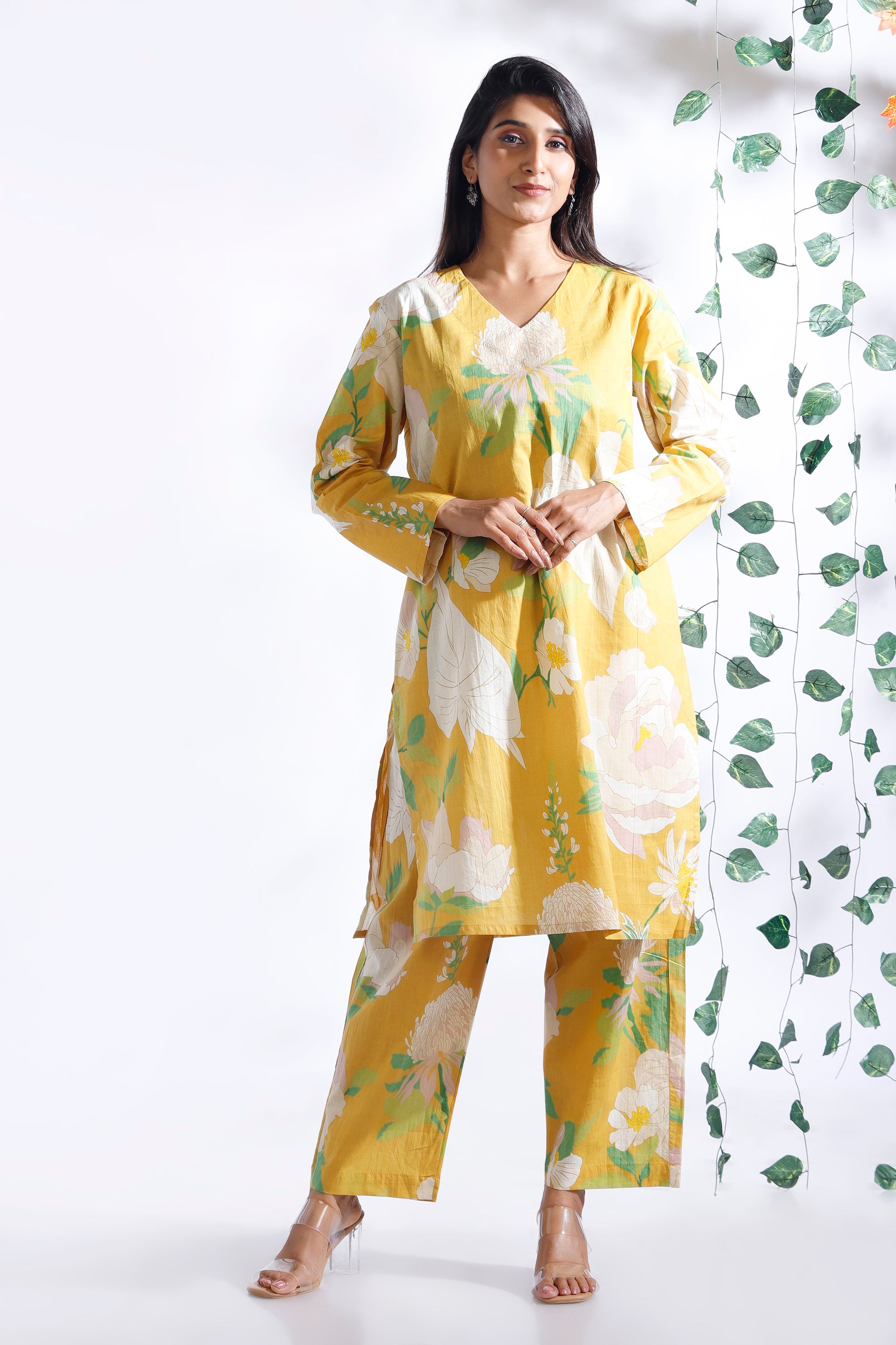 Woman wearing a yellow floral outfit against a white background with green leaf patterns.