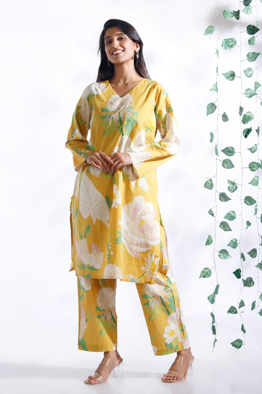 Woman wearing a yellow floral outfit standing next to a decorative plant on a white background