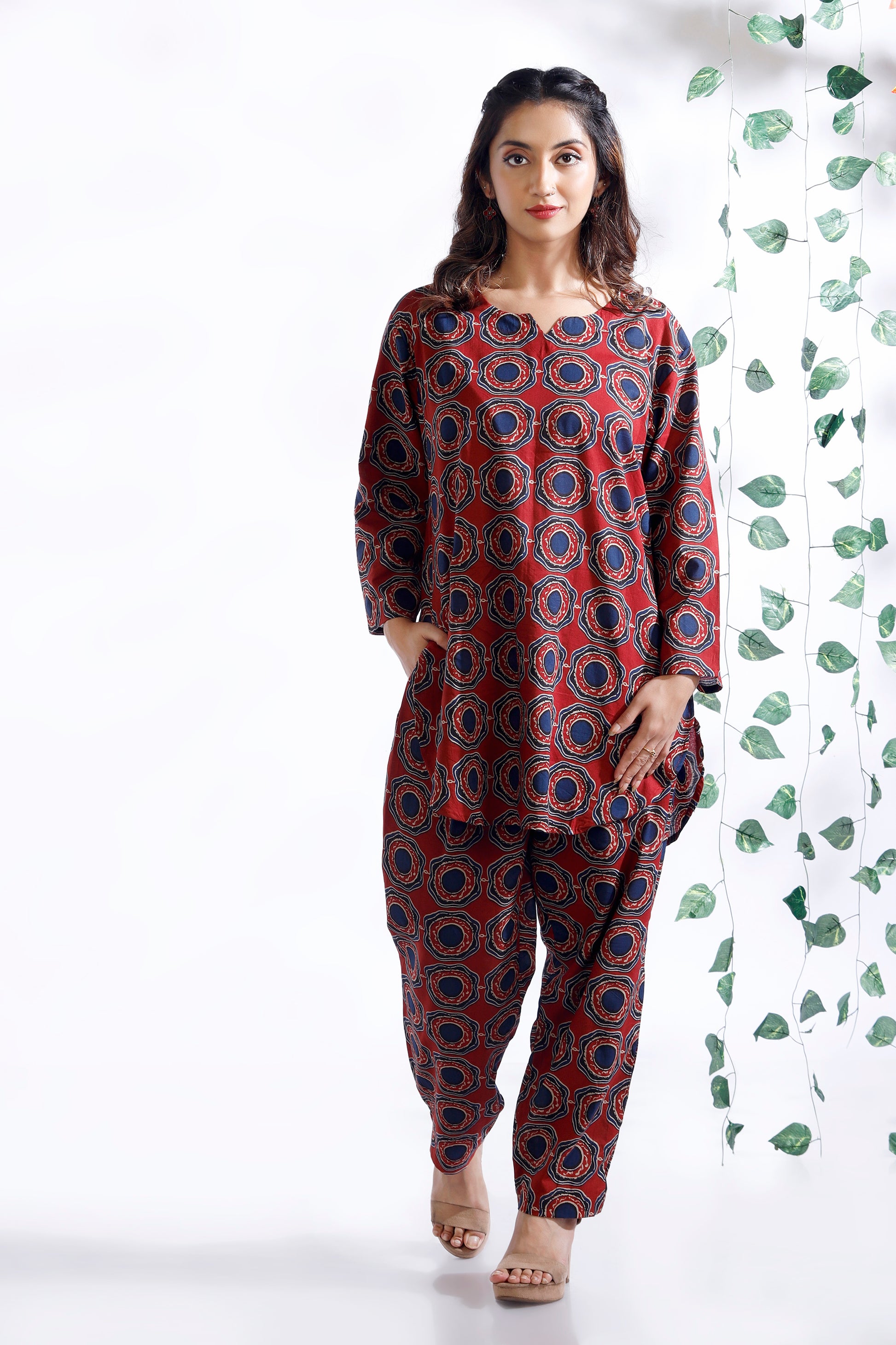 Woman wearing a red and blue patterned outfit against a white background with green leaves.