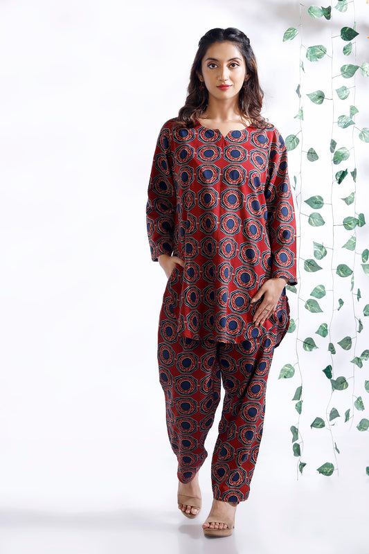 Woman wearing a red and blue patterned outfit against a white background with green leaves.