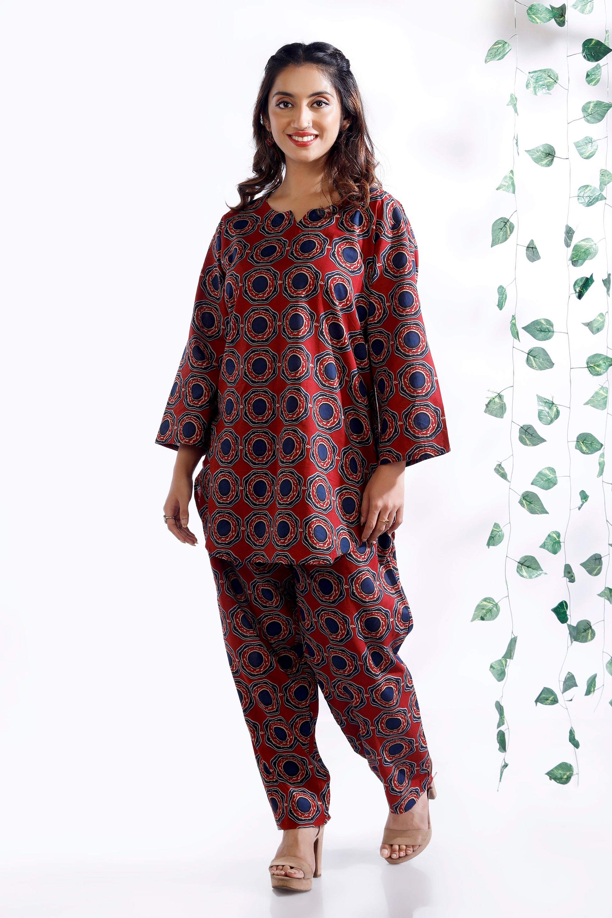 Woman wearing a red and blue patterned outfit on a white background with green leaves.