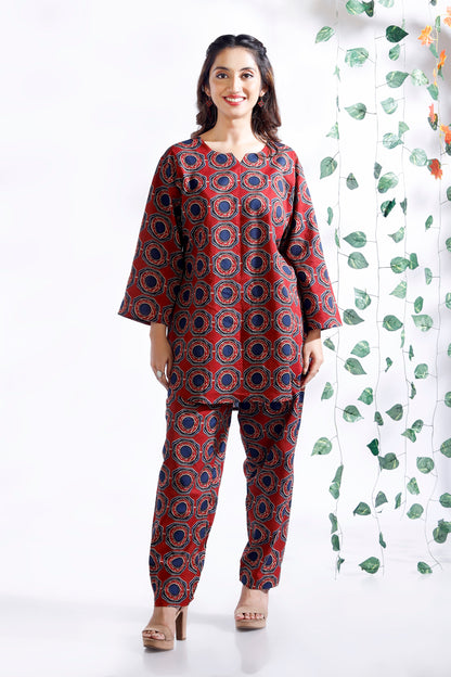 Woman wearing a red and blue patterned outfit standing against a white background with green leafy patterns.