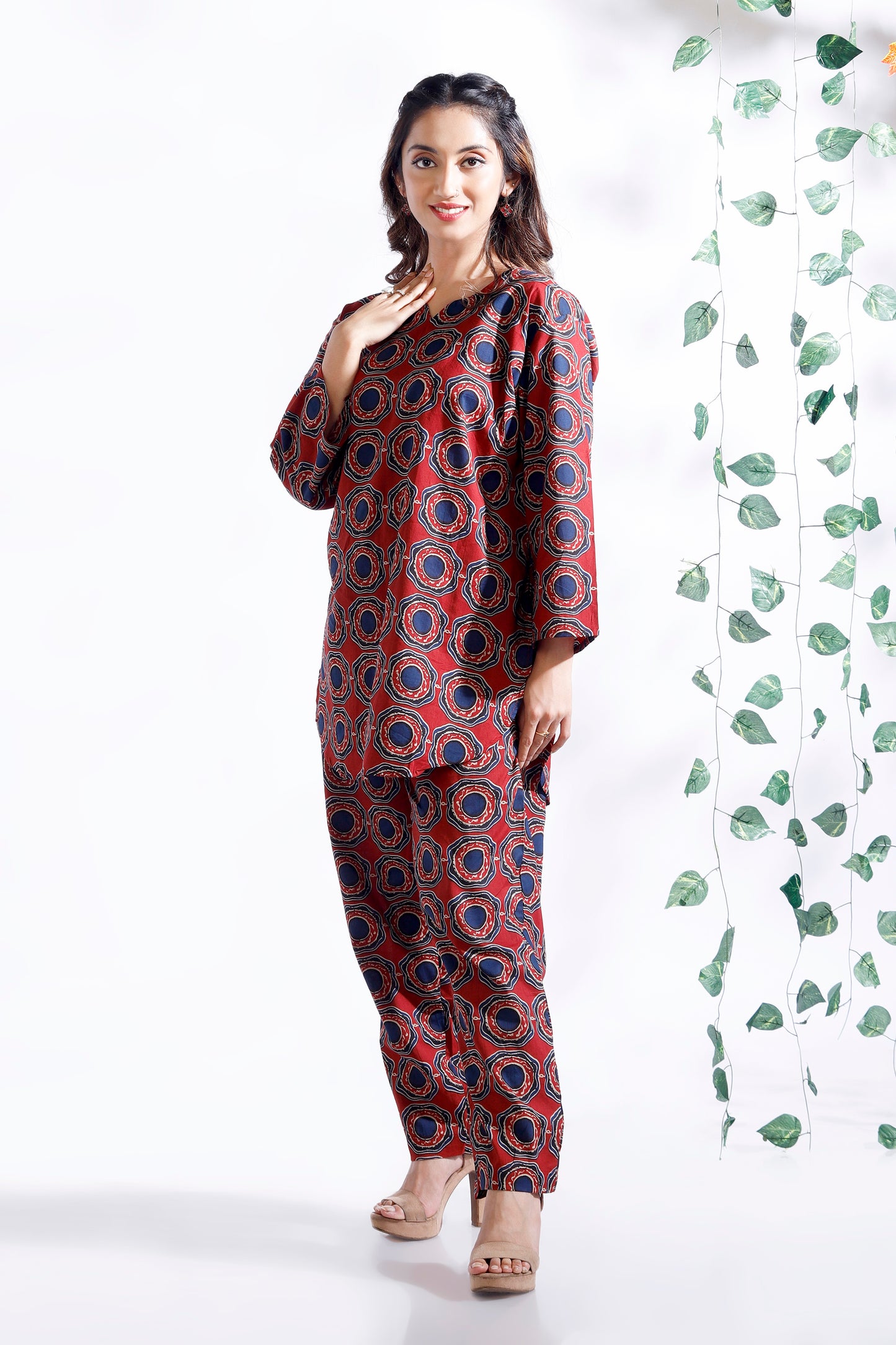 Woman wearing a red and blue patterned outfit standing next to a green leafy plant on a white background