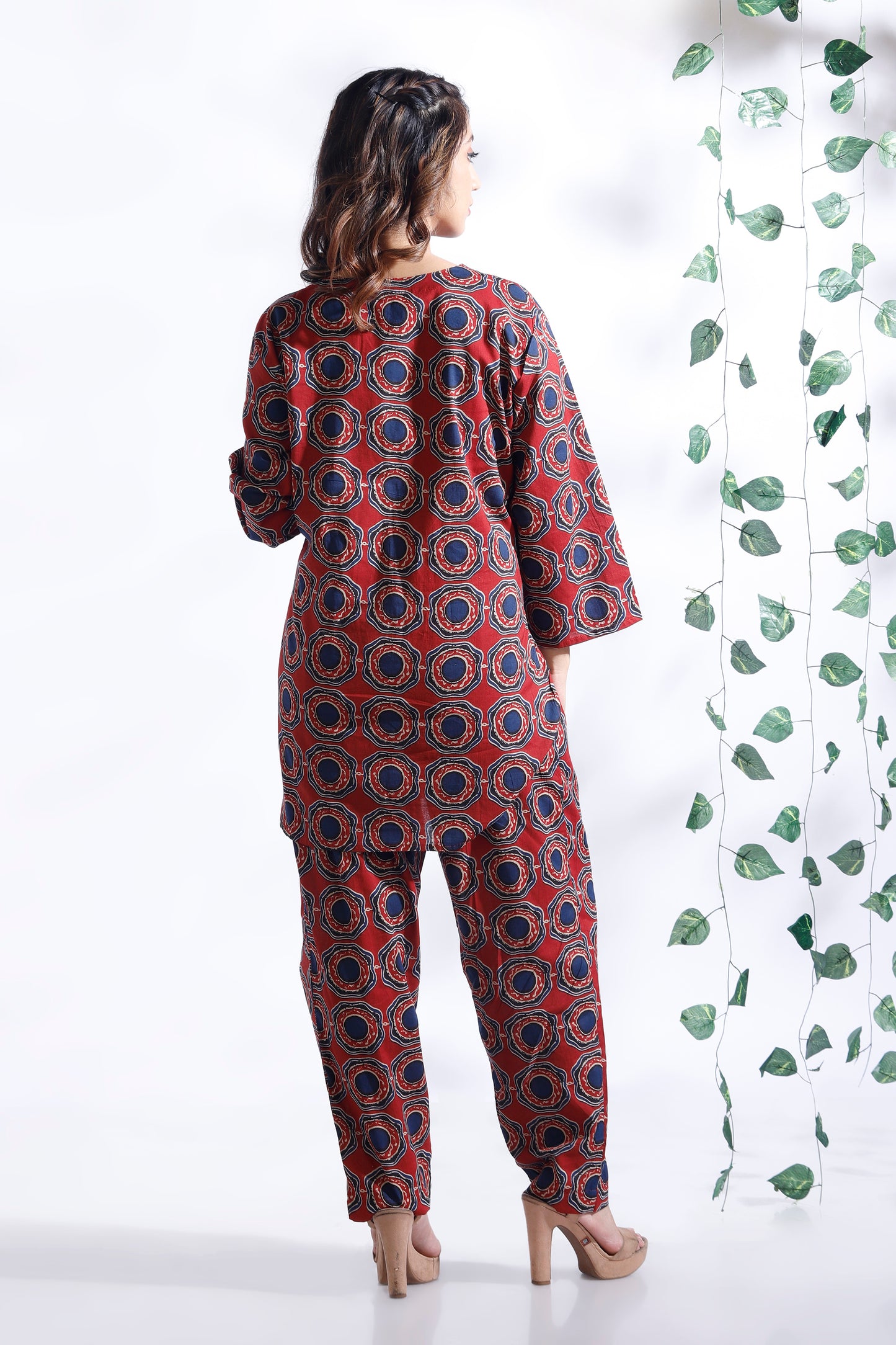 Woman wearing a red and blue patterned outfit with a white background and green leaves.
