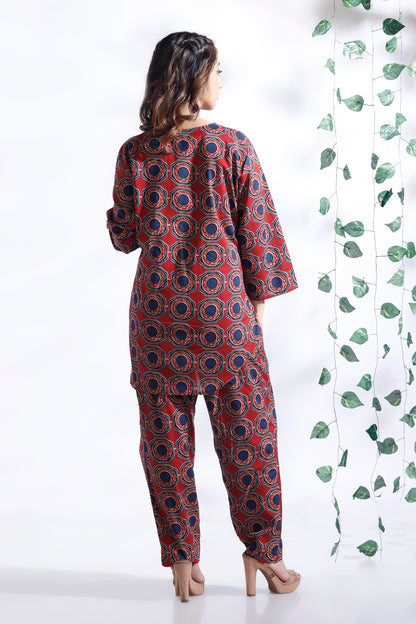 Woman wearing a red and blue patterned outfit with a white background and green leaves.