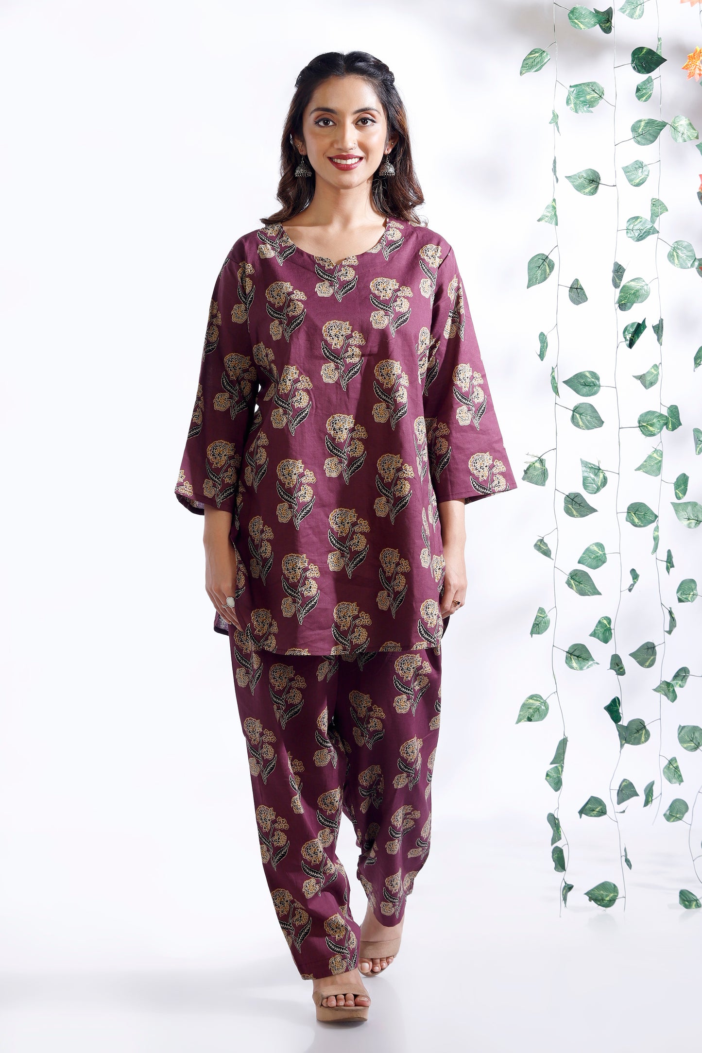 Woman wearing a purple floral outfit standing against a white background with green leaf patterns.
