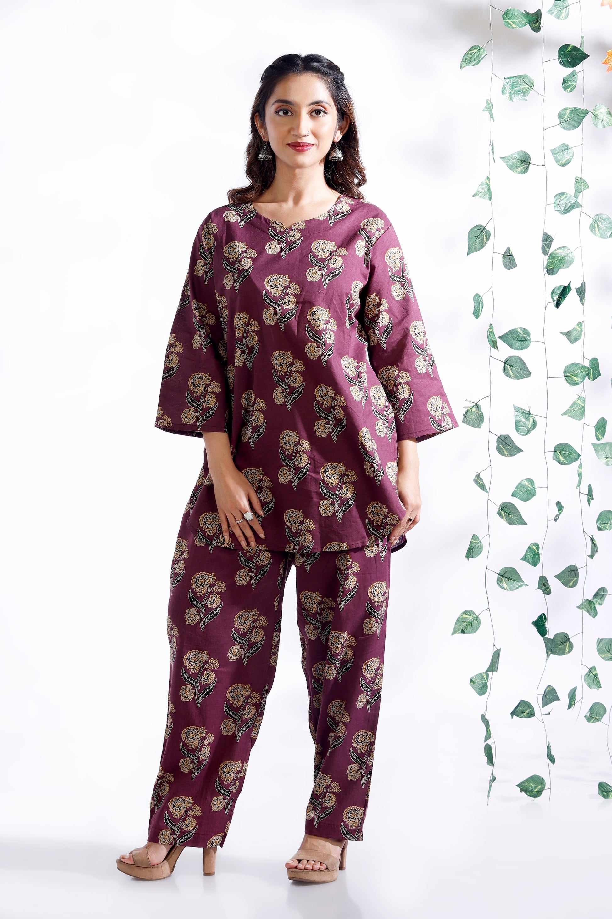 Woman wearing a purple floral outfit standing against a white background with green leaf patterns.