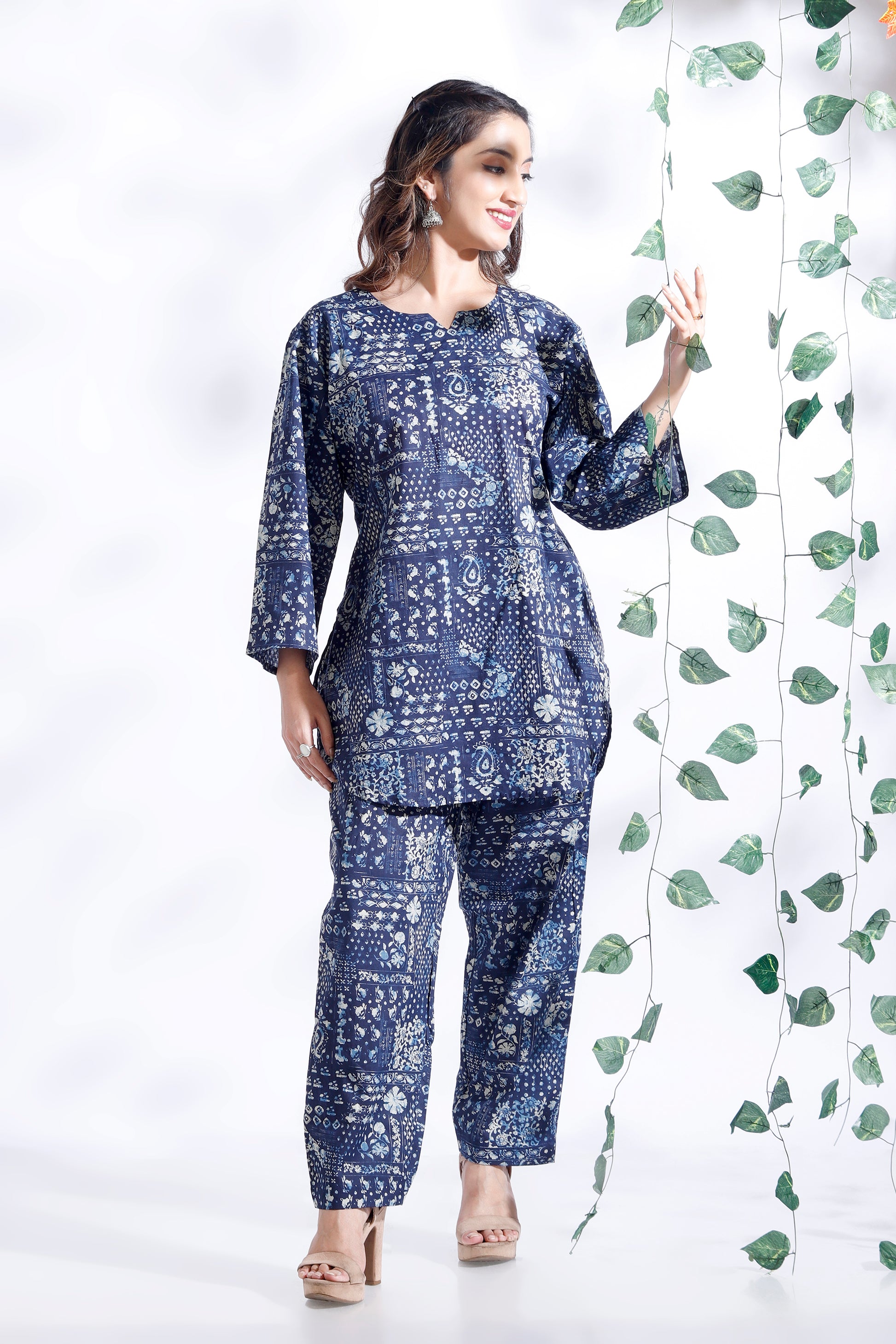 Woman wearing a blue patterned outfit standing next to green leaves on a white background