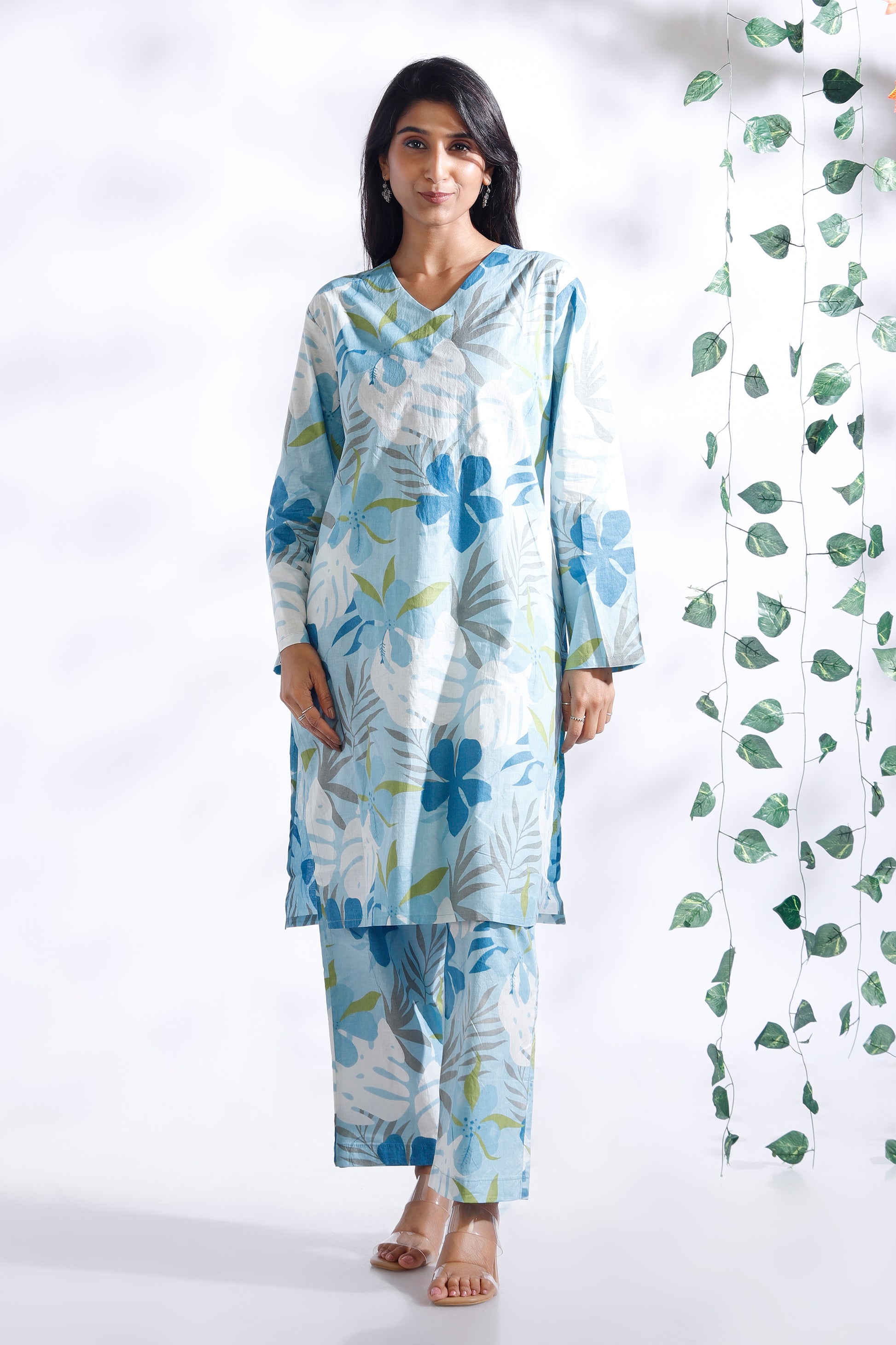 Woman wearing a floral dress with a white background and green leafy decoration.
