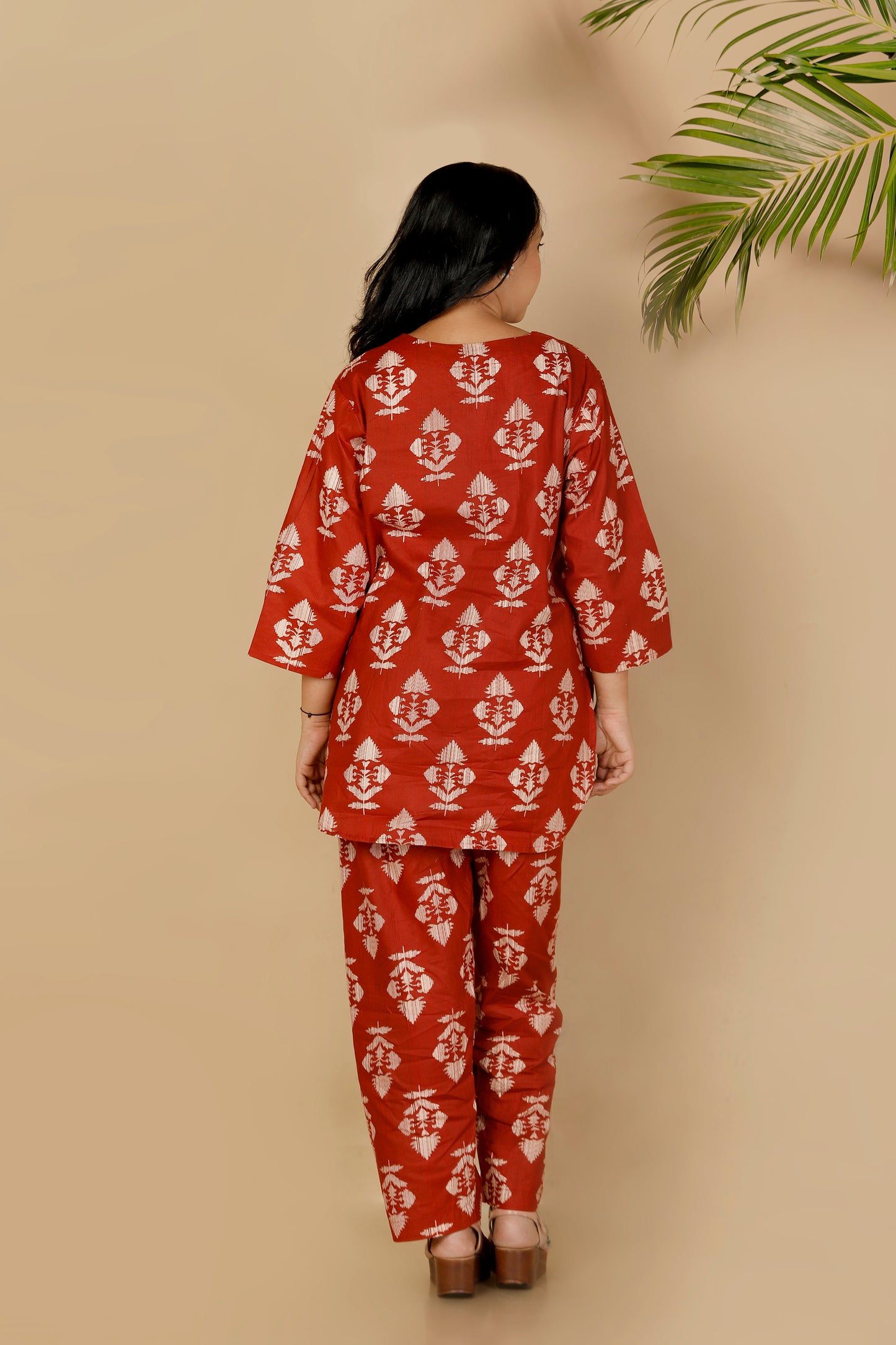 Woman wearing a red and white patterned outfit against a beige background with a palm leaf.