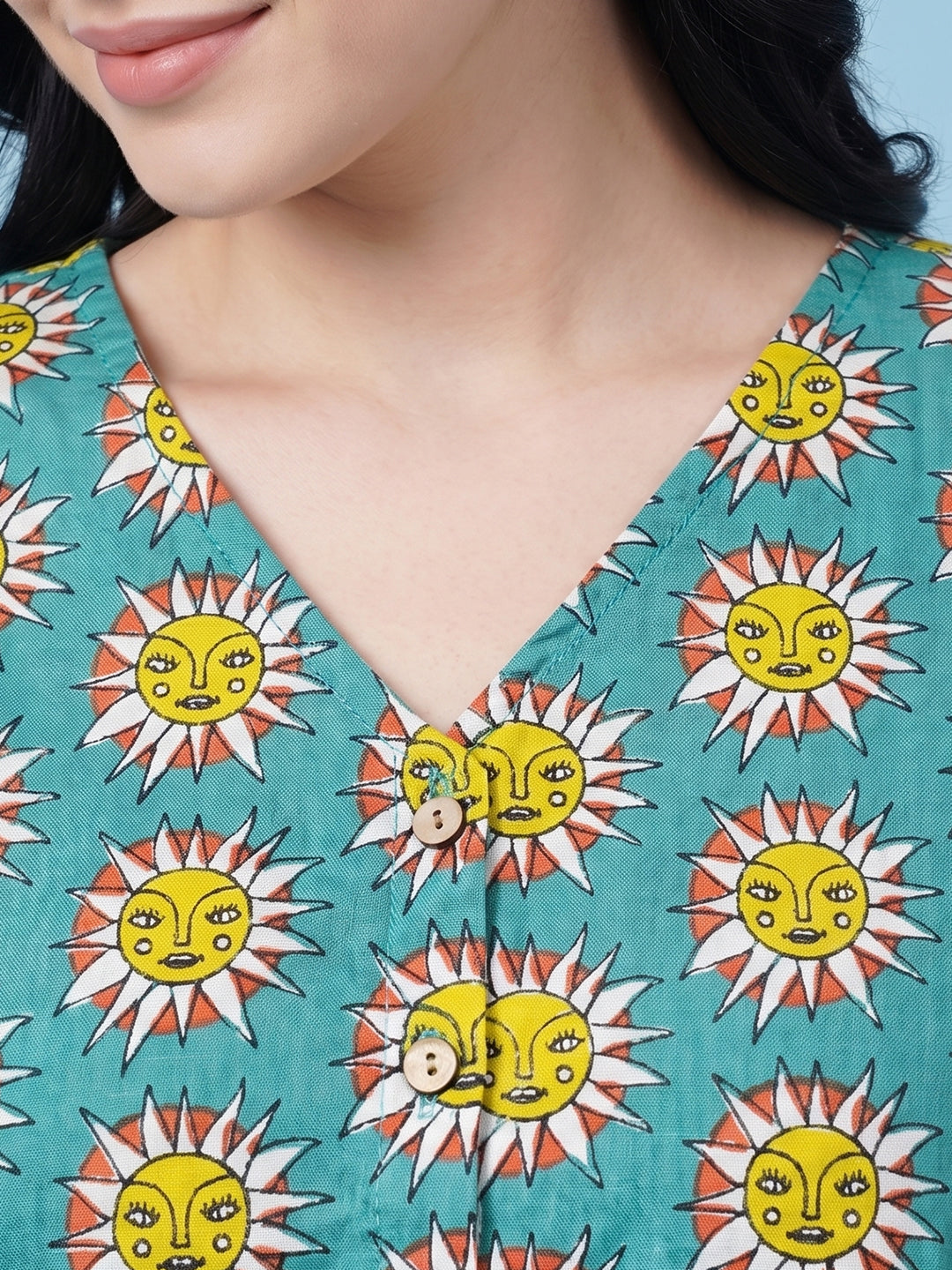 Close-up of a model wearing a teal V-neck top with a repeating yellow sun face pattern and wooden buttons.