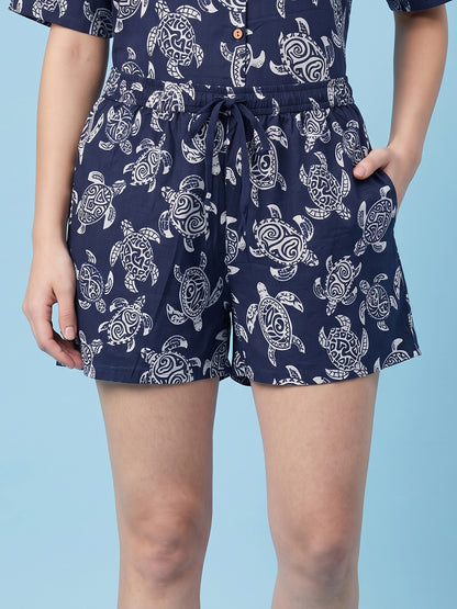 A person wearing navy blue shorts with a white sea turtle print, paired with a matching top, shown against a light blue background.