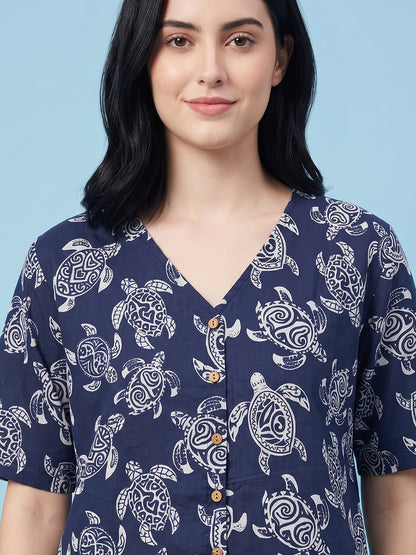 A woman wearing a navy blue short-sleeve button-up shirt with a white sea turtle pattern, set against a solid light blue background.